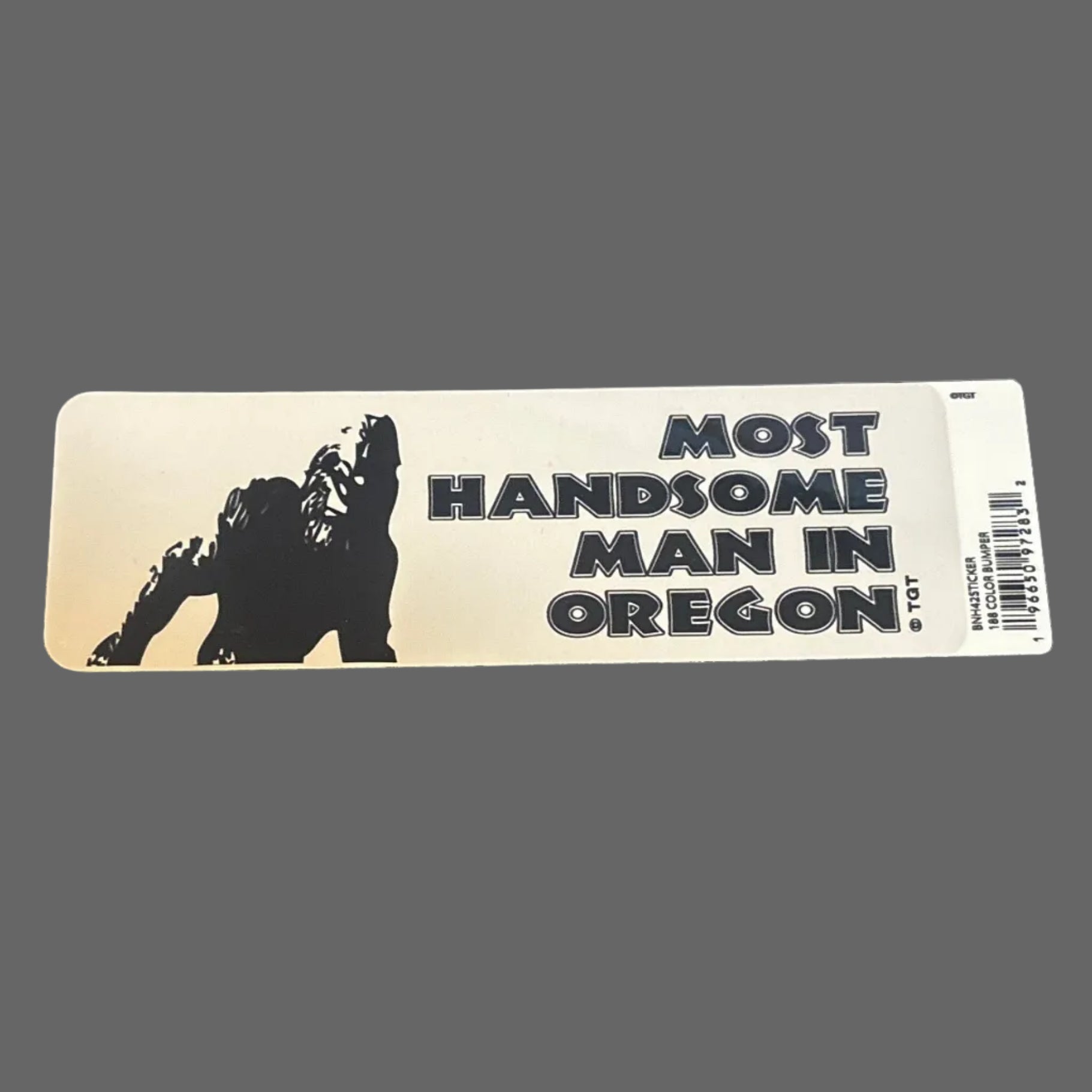 Sticker with 'Most Handsome Man in Oregon' text on a dark surface with a ruler and keyboard in the background.